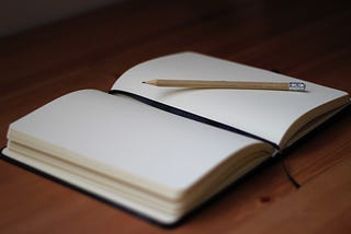 An open journal with a pencil sitting on a blank page