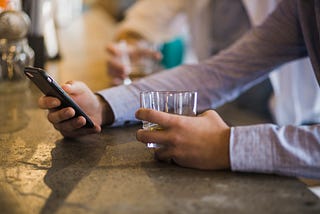 man at bar drink while using his phone