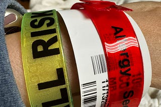 A wrist showing multiple hospital identification bands, including one for fall risk and another indicating allergies.