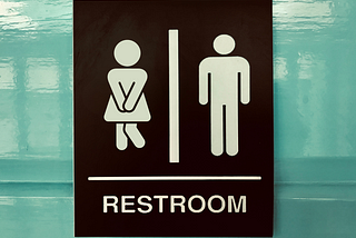 A restroom sign with a woman and man figure; woman is crossing her legs