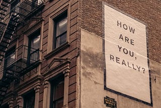 Quote painted on the side of a building reading: “How are you, really?”
