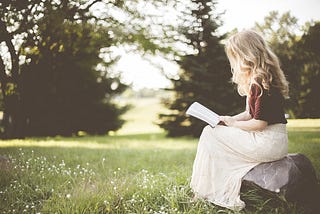 blonde woman reading a book in a field