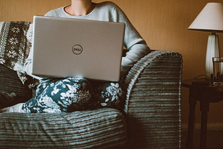 Image of a women sitting on a couch with a computer balanced on her knees
