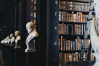 An old library filled with large books and white marble busts of historic men