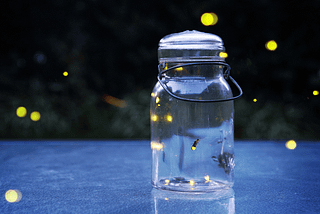 A large glass jar with small fireflies flying in and around it.