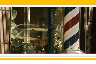 An antique barbershop pole in front of a barbershop. Old cars are reflected in the window of the barbershop.
