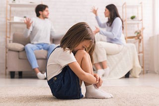 Young child listens as parents argue in background.