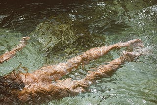 A pair of woman’s legs are seen swimming in a crystal clear body of water.