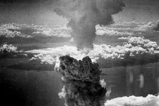 Billowing mushroom cloud rising over Nagasaki on August 9, 1945, captured from the air against a backdrop of scattered clouds.