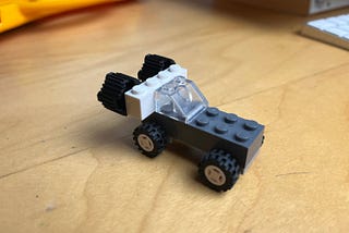 A small car made from a black Lego brick with two sets of wheels attached beneath it, a angled clear brick for window shield, and a white brick at the back, holding two round bricks that looked like jet engines, pointing at the back of the car
