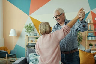 Older couple dancing together in a colorful living room, reflecting the emotional rewards and family connection often found in caregiving relationships. Photo by Vitaly Gariev on Unsplash