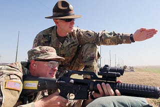 Drill sergeant instructing recruit on rifle range.