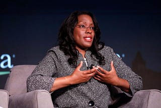 A Black woman speaking at a conference, sitting in a chair, Dana Peterson