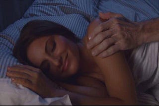 Horror movie still frame: a man’s hand touches a sleeping woman’s shoulder.