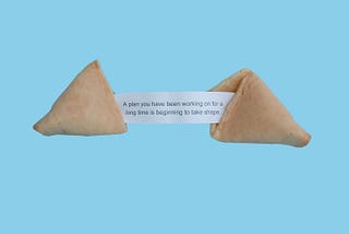 Fortune cookie split in half on a light blue background with a fortune reading: A plan you have been working on for a long time is beginning to take shape