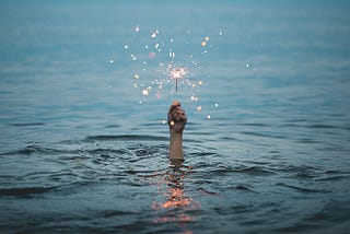 A hand lifts a lit sparkler out of the sea