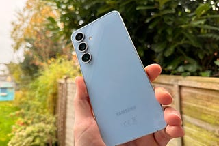 Blue Samsung S24 FE phone. The backdrop is a grassy scene.