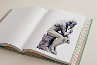 A book sits open. The page features an image of Auguste Rodin’s sculpture, The Thinker.