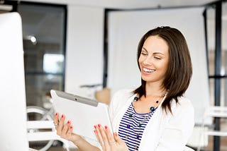 Professional-looking woman smiling as she looks at a tablet, presumably because it contains helpful information.