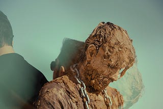 Mud-caked man with chain around his neck.