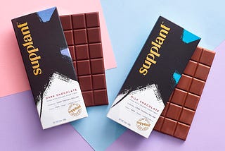 A dark chocolate bar and a milk chocolate bar on a pink and blue background.