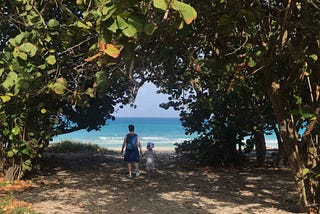 Mother and daughter walking through opening in trees to tropical beach in Varadero, Cuba