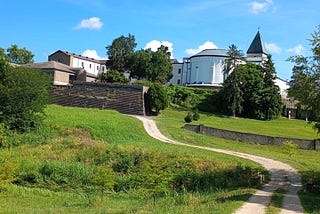 A side view of the outside of the rounded church and stone tower of the Abbey of Gethsemani along with one of the paths leading to the abbey, outside of Louisville KY.