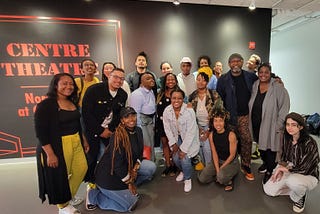 A diverse group of Groundwork Regional Lab participants posed in front of a black wall with words “Centre Theatre” printed on it in orange letters.