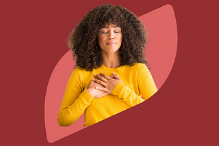 person with curly black hair wearing a yellow sweater holding bothhands to their heart. the background is dark and light red