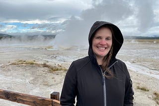 Jackie standing in black zipped hoodie in front of geyser.