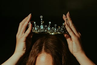 Woman putting a crown on her head.