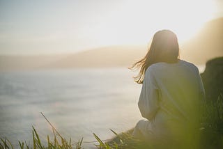 woman at sunset sitting looking out at the sea