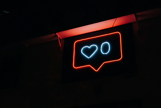 A red speech balloon neon sign containing two blue images of a heart and the number zero.