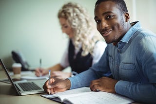 Business executive taking notes while using laptop