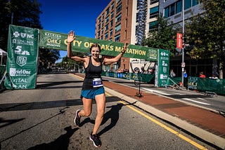 A female runner with arms raised celebrating at the finish line of a marathon