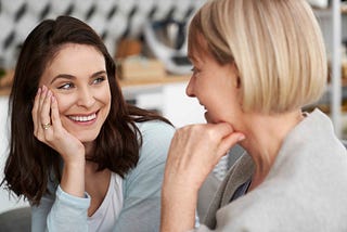 Two women of different ages smile and chat together warmly.