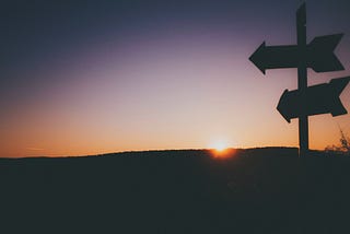 Silhouette of two signposts against a sunset