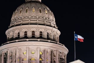 Texas flag blows in the wind after night falls on The Texas State Capitol Building in Austin.