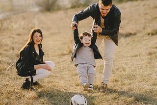Wife watching father playing soccer with his young son