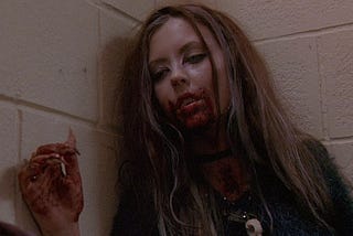 A scary young woman from a horror movie with blood on her face, shirt, and hand.