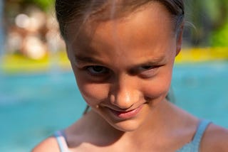 Close up photo of a girl in front of a swimming pool with a devious look on her face.