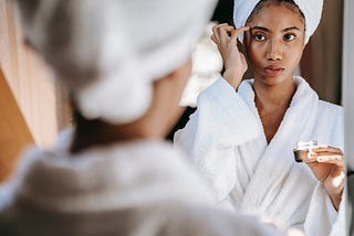 A young woman is applying niacinamide cream to her face while staring at her reflection in the mirror