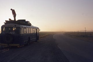 TWo young persons on top of a bus parked in a Afghanistan desert at dusk.