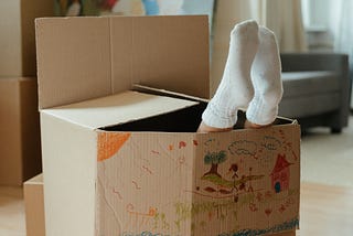child’s crayon drawing on outside of an open moving box with a man’s socked feet poking out