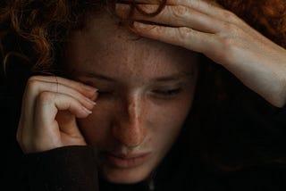 a sad woman gazing downward with one hand touching her forehead and the other wiping her eye