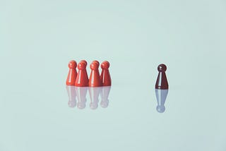 A group of red game pieces gather in a cluster, and one brown piece is set apart.