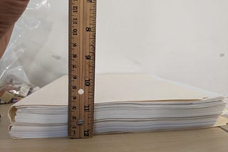 two manila folders stacked vertically, with a ruler measuring their thickness