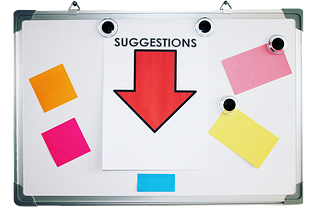 A whiteboard with orange, yellow, pink, and blue sticky notes on it and a paper with a red arrow that reads suggestions.