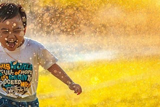 A joyous boy running through a spray of water.