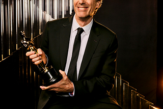 Walter Salles, de terno e gravata, sorridente, posa segurando ao estatueta dourada do Oscar que conquistou na categoria de Melhor Filme Internacional por “Ainda Estou Aqui”